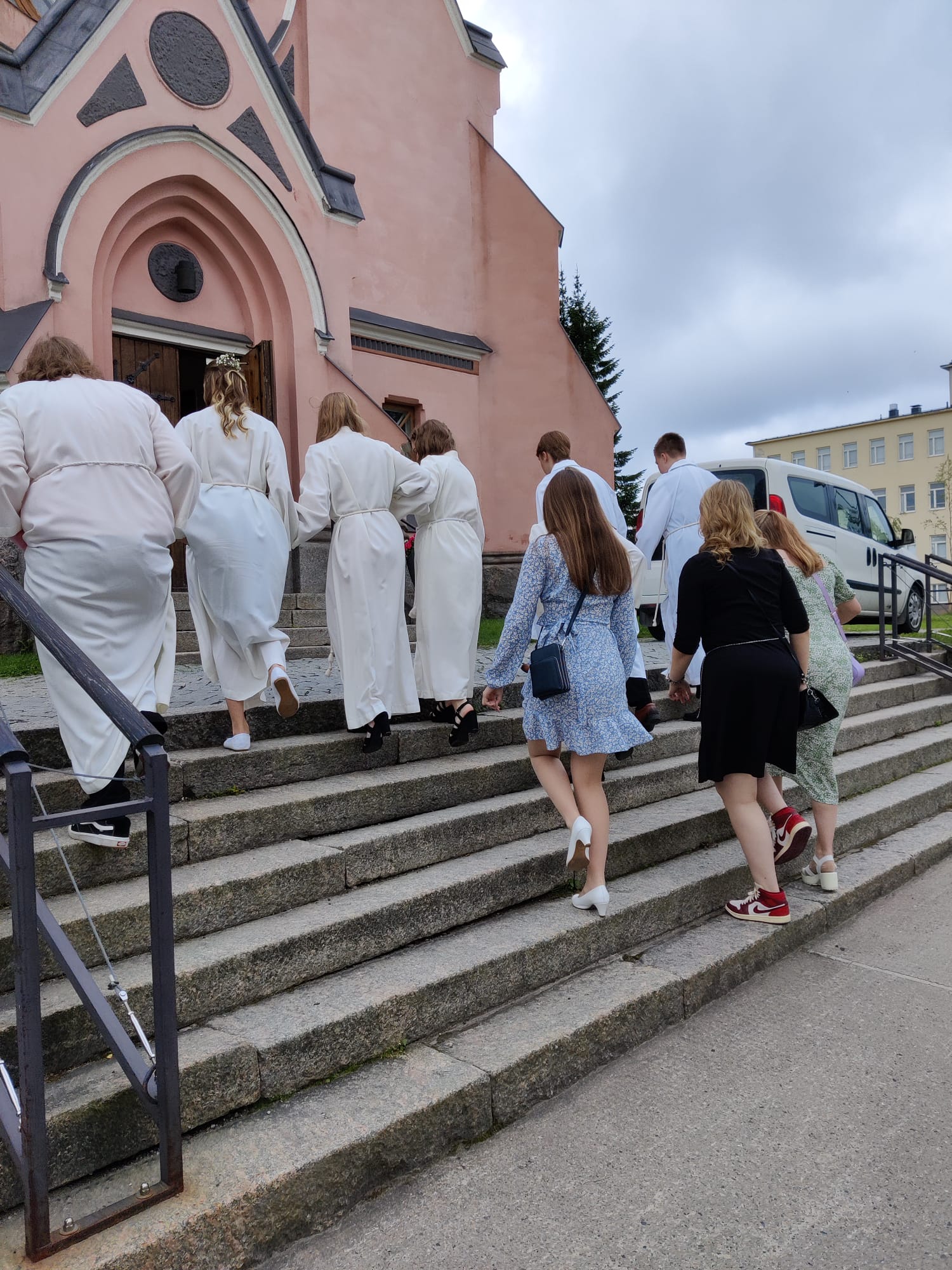 Konfirmoitavat nuoret ovat matkalla kohti kirkkoa. Nousevat portaita kuvassa.