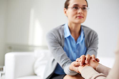 Nainen joka lohduttaa toista pitämällä käsistä kiinni